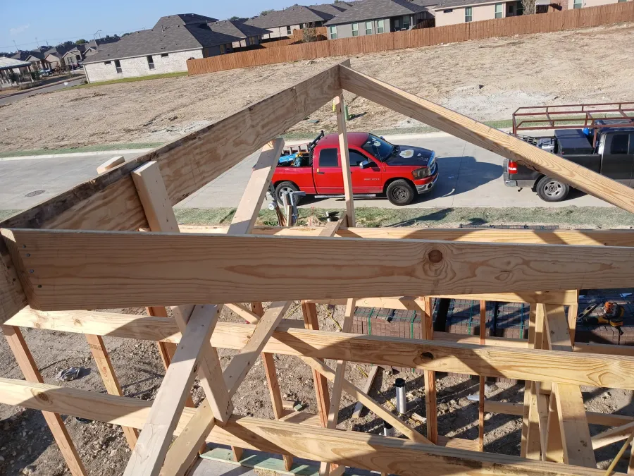 Gable truss standing over a framed garage with work trucks on the street