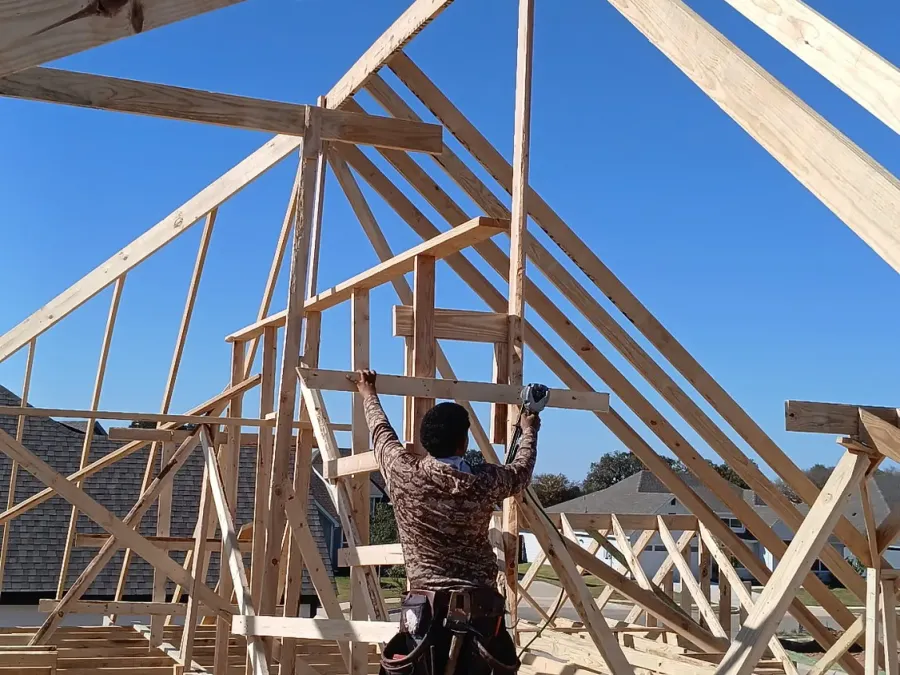 Carpenter nailing off roof trusses on a new house frame under a clear sky